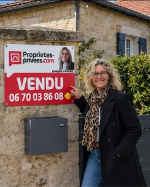 Josepha Favard devant le panneau VENDU d’une maison en pierre de taille, au portail